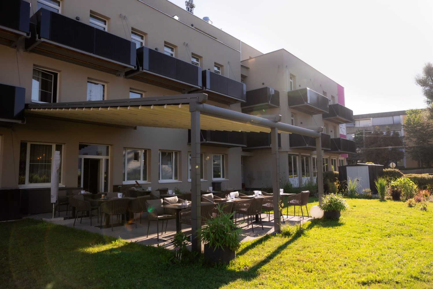 Frühstücksbereich im Garten des HOTEL max70 mit schattiger Terrasse und gemütlichen Sitzmöglichkeiten.