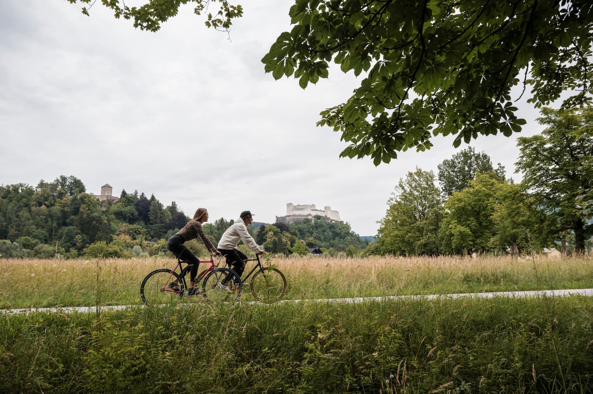 Radfahrer in Salzburg mit der Festung Hohensalzburg im Hintergrund, umgeben von historischer Kulisse.